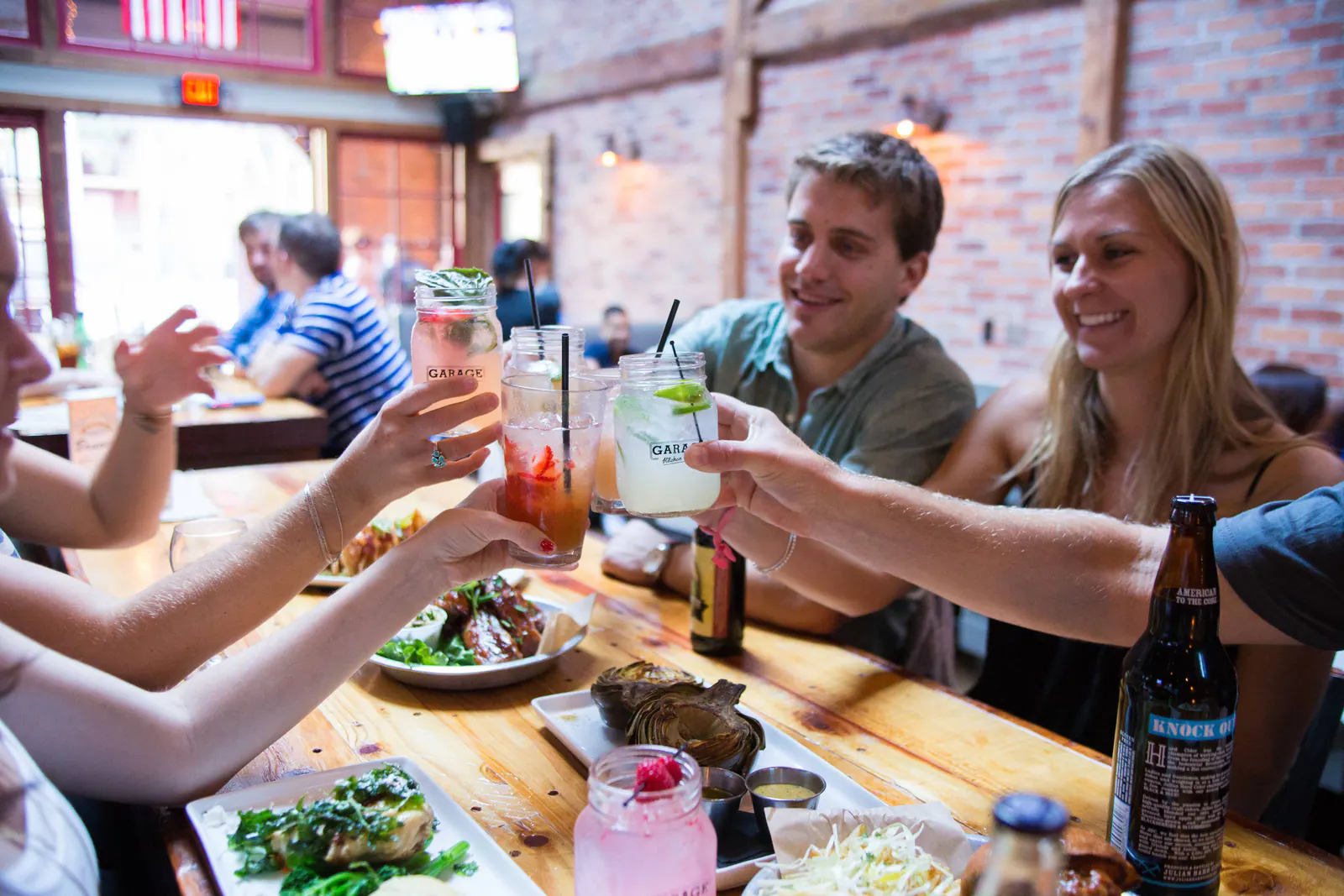 Friends toasting colorful cocktails while dining together at Garage Kitchen + Bar