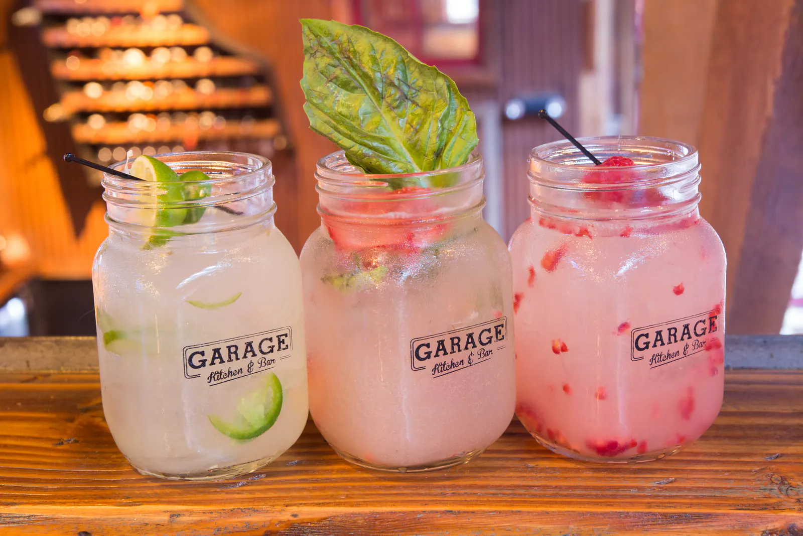 Close-up of three branded mason jar cocktails garnished with lime, basil and raspberry