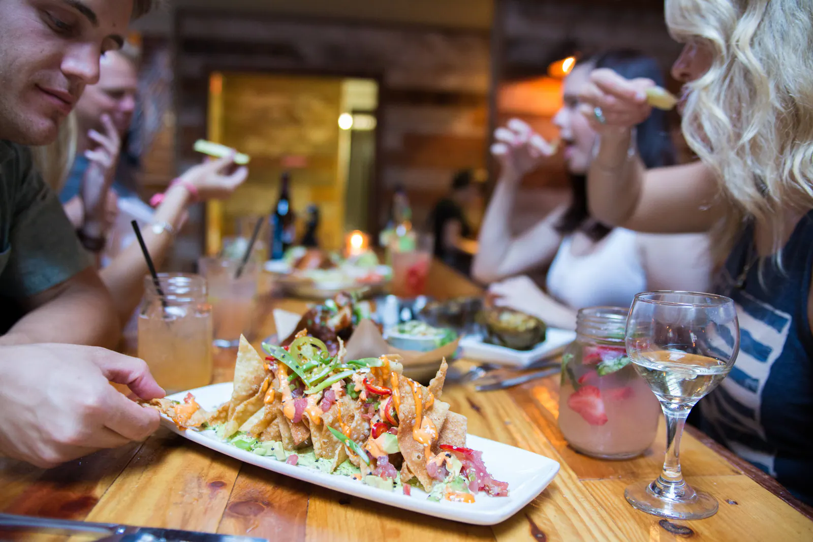 Friends sharing wonton nachos and cocktails at a wooden restaurant table