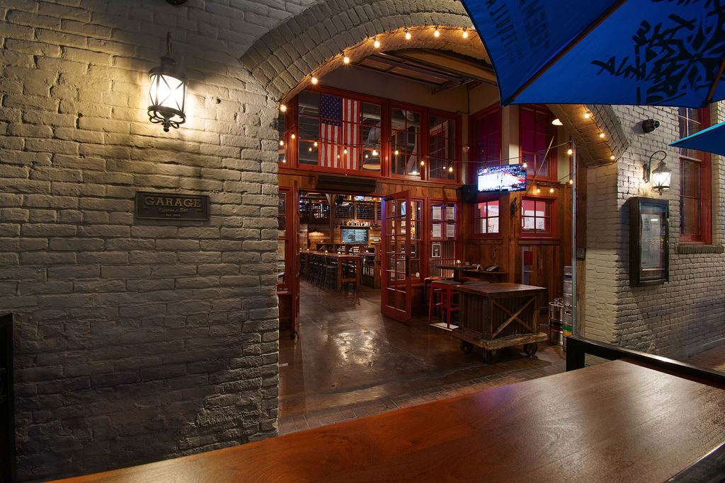 Arched entrance to Garage Kitchen + Bar with open red doors and patio tables